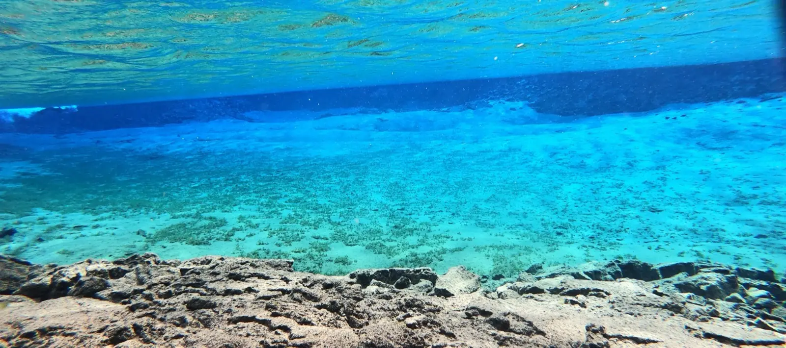 Underwater view of sunlit, crystal-clear turquoise water over pale stones at Silfra, Iceland